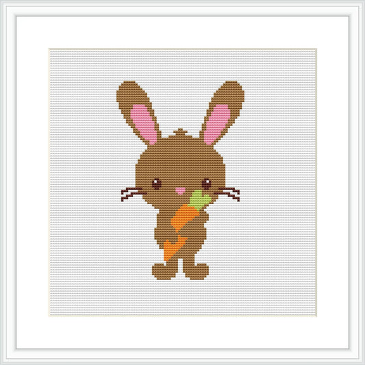 The image shows a framed cross stitch pattern of a cute brown bunny with pink inner ears standing upright. The bunny is holding a carrot with green leaves in its front paws. The background is white, and the stitching is visible.