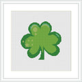 A cross stitch pattern featuring a green four-leaf clover centered on a white background, framed in a simple square pattern.