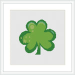 A cross stitch pattern featuring a green four-leaf clover centered on a white background, framed in a simple square pattern.