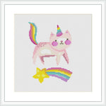 The image features a framed cross-stitch pattern depicting a pink 'caticorn'—a mythical creature that's a blend between a cat and a unicorn. The caticorn has a multicolored tail and horn, and is positioned above a shooting star and a rainbow.