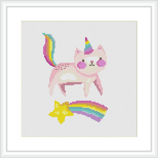 The image features a framed cross-stitch pattern depicting a pink 'caticorn'—a mythical creature that's a blend between a cat and a unicorn. The caticorn has a multicolored tail and horn, and is positioned above a shooting star and a rainbow.