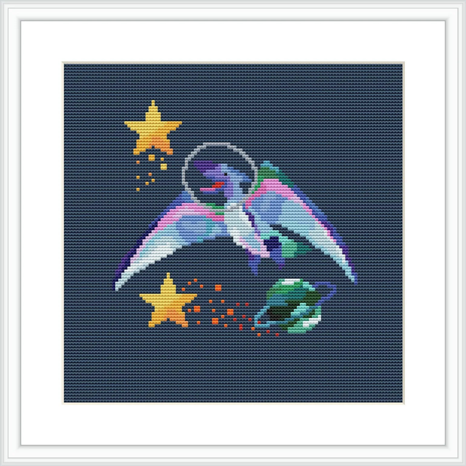 The image depicts a cross stitch pattern featuring a cartoon dinosaur wearing a space helmet and drifting through space with stars and a constellation around it.