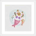The image displays a framed cross stitch pattern of a cat with mermaid tail and fins, holding a seashell and a jellyfish, with a stylized underwater backdrop including bubbles and a coral branch.