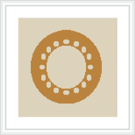 The image displays a framed cross stitch pattern hanging on a wall. The design depicts a centered circular motif made up of small geometric shapes, predominantly in shades of yellow, on an ecru or light beige aida cloth.