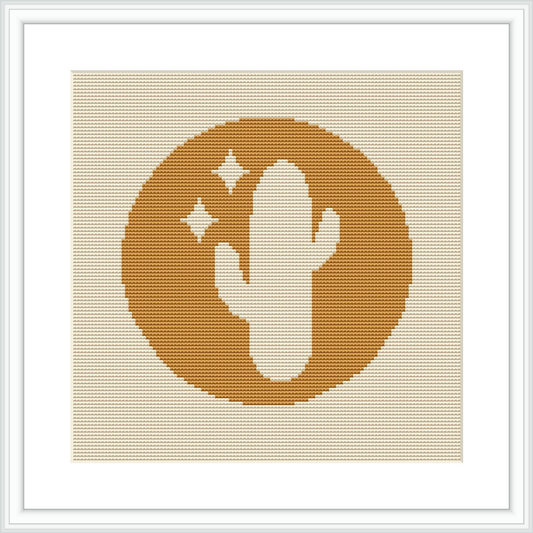 The image showcases a cross stitch pattern framed in white, depicting a centered stylized cactus within a circular motif on a geometrically patterned warm-toned background.