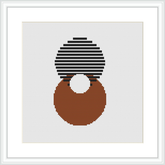 The image shows a framed cross stitch pattern with a white background, featuring an abstract design composed of two overlapping circles, one on top of the other rendered in stripes of black and white, and the other solidly filled with shades of brown placed on a grid indicative of a 112 by 112 stitch count.