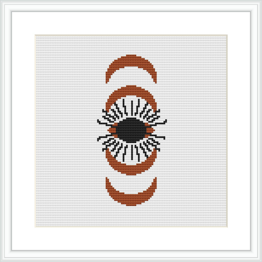 A cross stitch pattern featuring an eye framed by two crescent shapes on a white canvas. The design is composed of brown, beige, black, and orange colors.