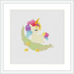 The cross stitch pattern depicts a stylized unicorn with a multicolored mane and tail, sitting on a crescent moon-like cloud. A small rainbow with stars around it is presented behind the unicorn. The embroidery is framed in a simple white frame with a white matte border.