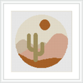 A framed cross stitch pattern showing a stylized desert scene with a cactus, rolling hills and a setting sun within a circle, all rendered in a pixel-like geometric style.