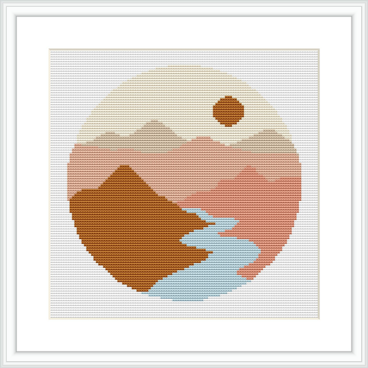 The image displays a circular cross stitch pattern depicting an abstract mountain landscape with a river, enclosed within a graphical circular border. The foreground shows a brown mountain, the middle ground a smaller pink mountain, and in the background, a rising or setting sun in a light beige sky, all framed by a white border.