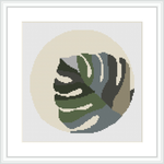The image displays a framed cross stitch pattern of a Monstera leaf set against a cream-colored, circular background, surrounded by a white border.