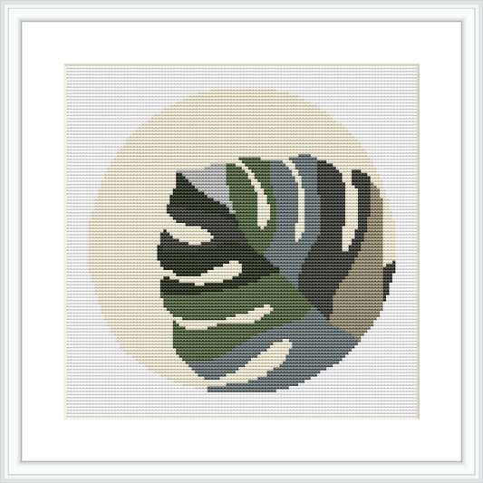 The image displays a framed cross stitch pattern of a Monstera leaf set against a cream-colored, circular background, surrounded by a white border.