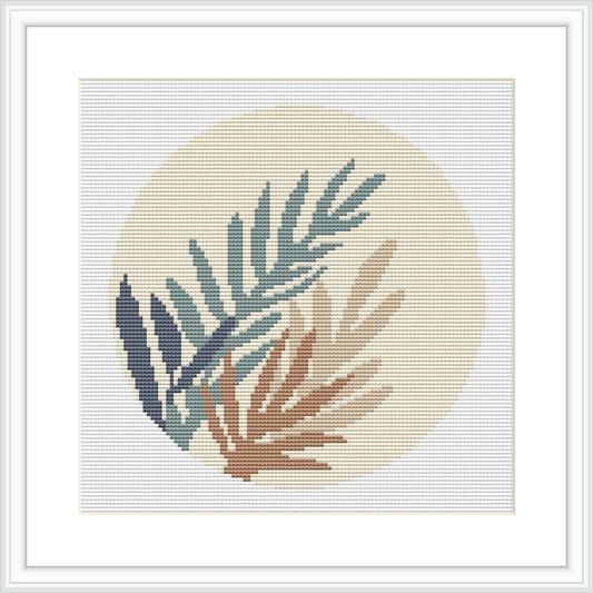 A cross stitch pattern featuring a collection of fern leaves in various shades of green and tan, arranged in a circular gradient on a cream-colored background, encased within a light frame.