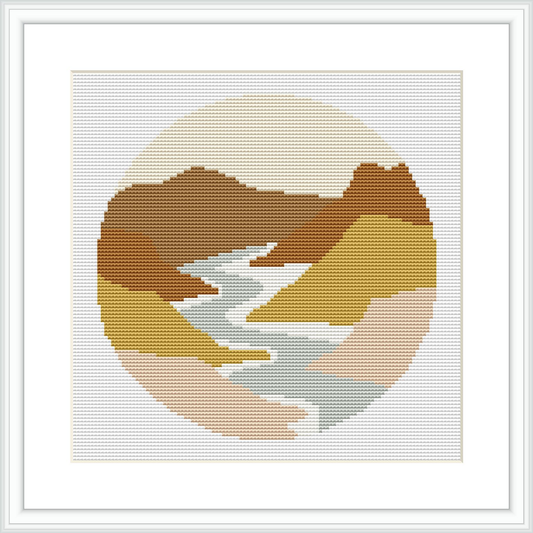 A cross stitch pattern featuring a circular depiction of a river landscape with surrounding mountains. The colors transition smoothly to create a harmonious image. The design is contained within a circular border and presented in a white frame.