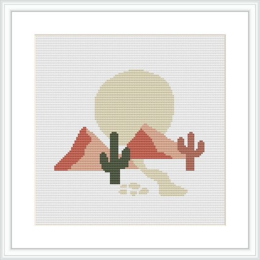 The image depicts a cross stitch pattern featuring a desert scene with two cacti in the forefront, and mountains with a large setting sun in the background, all framed within a white border.