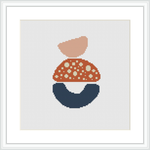 The image displays a cross stitch pattern framed in a white square frame against a white background. The pattern itself consists of three abstract shapes stacked to resemble a simplistic house or dwelling, with the topmost shape colored salmon pink, followed by a coral shade with white polka dots, and a navy blue base that suggests stability.