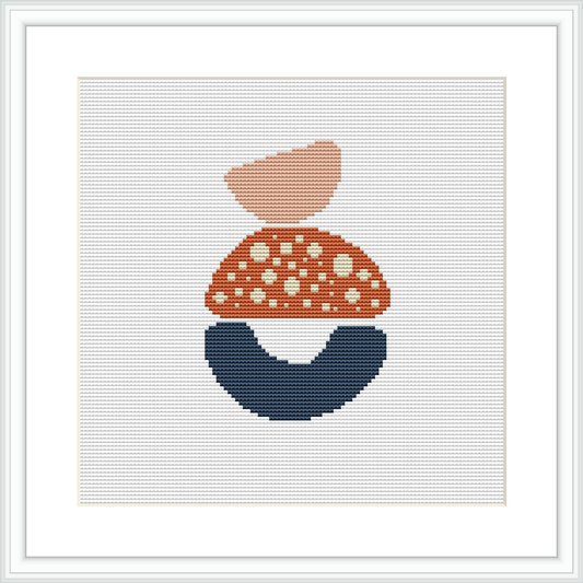 The image displays a cross stitch pattern framed in a white square frame against a white background. The pattern itself consists of three abstract shapes stacked to resemble a simplistic house or dwelling, with the topmost shape colored salmon pink, followed by a coral shade with white polka dots, and a navy blue base that suggests stability.