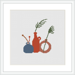 Three earthenware vessels of varying shapes and sizes, each containing green plant sprigs, are depicted against a plain background on a cross stitch canvas. The piece is framed in a simple white frame.