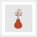 The image depicts a cross stitch pattern featuring a crimson red vase with a handful of white blooms and sprigs of green leaves, all set against a plain white background within a square frame.