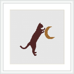 The image features a cross stitch pattern of a brown cat standing on its hind legs, left paw extended upwards, touching a crescent moon. The background is a plain white fabric, framed by a simple white frame, suggesting a wall art decor.