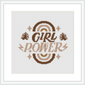 The image showcases a framed cross stitch sampler with the words 'GIRL POWER' in a bold font at the center, surrounded by ornamental floral elements and accents in shades of brown.