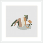 The image displays a framed cross-stitch pattern featuring an abstract representation of a woman sitting in a relaxed pose with a leaf-like pattern in the background.