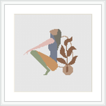 This image showcases a framed cross stitch pattern. It features an abstract silhouette of a woman with an earthy-toned leaf motif. The figure is centered within the square frame, set against a plain white background.