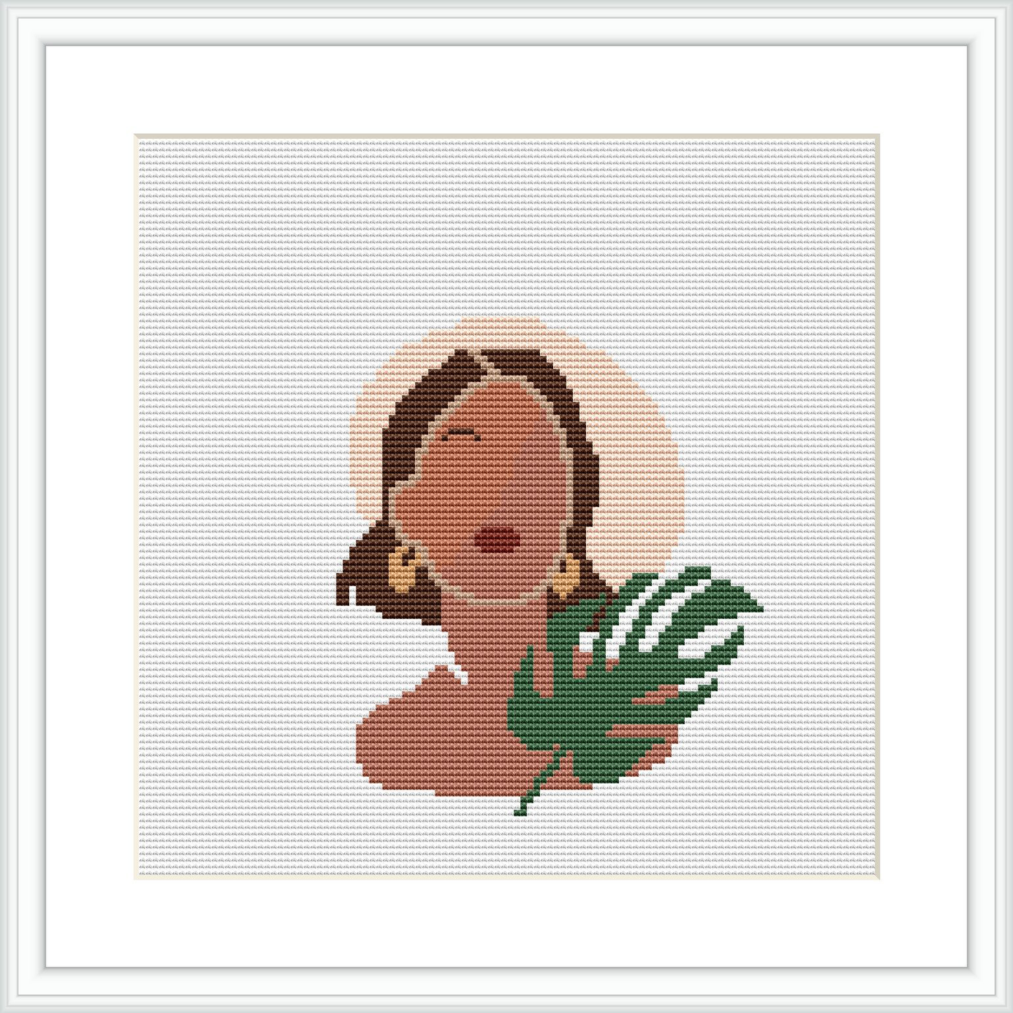 The image shows a framed cross stitch pattern. The pattern depicts a woman's profile with closed eyes and a serene expression. She appears to be wearing a large, round earring and there is a stylized tropical leaf beside her. The background is plain, allowing the figure to stand out.
