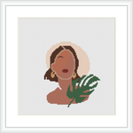 The image shows a framed cross stitch pattern. The pattern depicts a woman's profile with closed eyes and a serene expression. She appears to be wearing a large, round earring and there is a stylized tropical leaf beside her. The background is plain, allowing the figure to stand out.