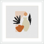 A framed cross stitch pattern depicting an abstract representation of a female silhouette with elements in black, beige, and terracotta colors, against a white background within a square frame.