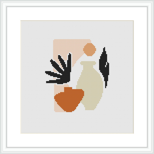 A framed cross stitch pattern depicting an abstract representation of a female silhouette with elements in black, beige, and terracotta colors, against a white background within a square frame.