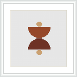 The image shows a framed cross stitch pattern with a central abstract geometric design consisting of a larger, inverted trapezoid stacked upon a smaller one, flanked by two smaller circles, all in various shades of brown on a white background.