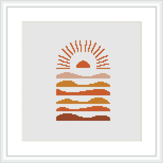 The cross stitch pattern depicts an abstract desert scene with a stylized sun above layered hills or sand dunes, arranged in a geometric gradient style.
