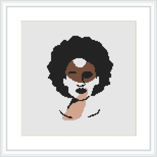 The image displays a framed cross stitch pattern hung on a wall. The design features an abstract illustration of a woman's face with geometric shapes and a limited color palette.