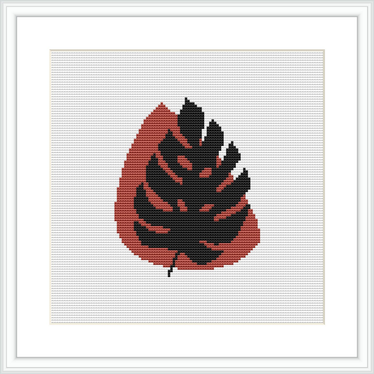 A framed cross stitch pattern depicts an abstract design resembling a leaf with a combination of crimson and black, highlighted with pale pink, against a white background.