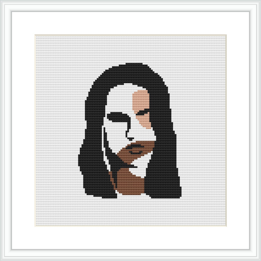 The image depicts a framed cross stitch pattern featuring an abstract design of a woman’s face. The face is stylized with geometric shapes and a limited color palette, focusing on shades of black, white, gray, and hints of beige and brown.