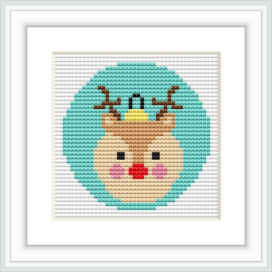 This is an image showcasing a cross stitch pattern framed in a white square frame, with the cross stitching done on fabric. The center of the design features a stylized reindeer with a red nose and a crown, set against a light blue background encircled by a green border.