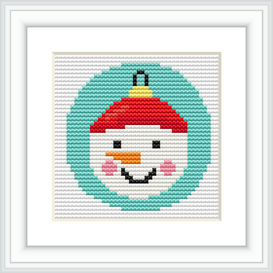 The image depicts a framed cross stitch pattern of a snowman's face with a red and green hat, centered within a circular border. The snowman is smiling and appears on a light grey aida cloth. The frame is white with a rectangular shape and a textured matting around the design.