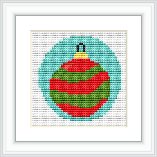 The image shows a framed cross stitch pattern of a Christmas bauble. The bauble is primarily striped with red and green, has a gold-colored top, and is centered on a white canvas surrounded by a simple white frame.