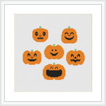 The image shows seven cross-stitched pumpkins with varying facial expressions aligned in a grid-like formation against a white fabric background. Each pumpkin is predominantly orange with black detailing for the eyes, nose and mouth, and a small patch of green at the top to represent the stem.