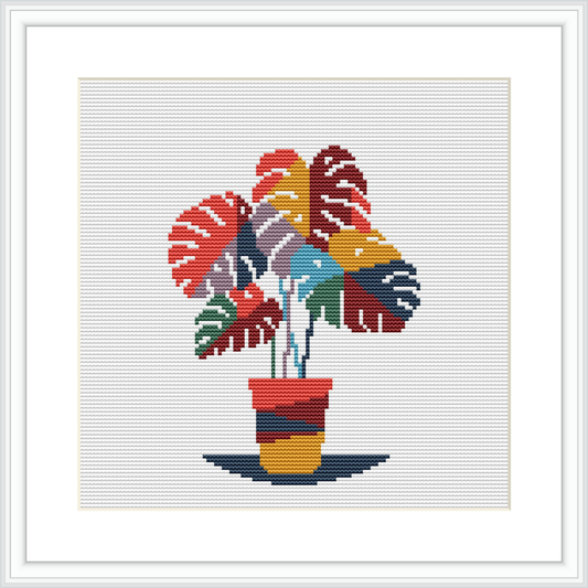 The image depicts a cross stitch pattern of a monstera plant with multicolored leaves in a striped pot, framed by a simple black border on a white background.