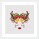 The image displays a framed cross stitch pattern of a stylized deer face with festive decorations. The deer's antlers are embellished with holly and ornaments. The design is centered on a white cloth background, and the stitches are finely done, capturing the essence of the Christmas holidays.