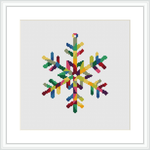 A framed cross stitch pattern depicting a colorful geometric snowflake on a white background, encased in a square frame.