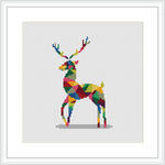 The image showcases a cross stitch pattern of a stylized deer composed of multicolored geometric shapes, framed and presented on a white background for display.