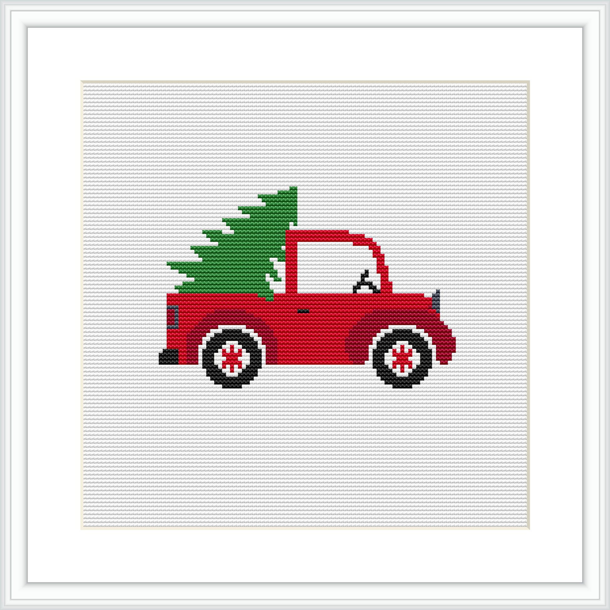 The image shows a cross stitch pattern of a red vintage truck viewed from the side, carrying a green evergreen tree on the back. The pattern is framed by a simple white border and the picture is presented as if it is within a white frame against a light background.