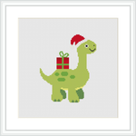 A green dinosaur standing upright with a red and white striped festive hat on its head and a wrapped gift with a gold bow on its back, all stitched on a white canvas.