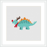 The image depicts a cross-stitch pattern of a green dinosaur with a red scarf and what appears to be reindeer antlers, embellished with decorative Christmas-themed patterns.