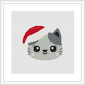 The image showcases a cross stitch pattern framed in white. It features a cute grey cat's face with black and white details and pink cheeks, wearing a red Santa hat. The background is plain white.