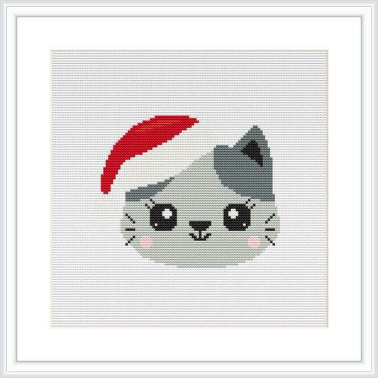 The image showcases a cross stitch pattern framed in white. It features a cute grey cat's face with black and white details and pink cheeks, wearing a red Santa hat. The background is plain white.