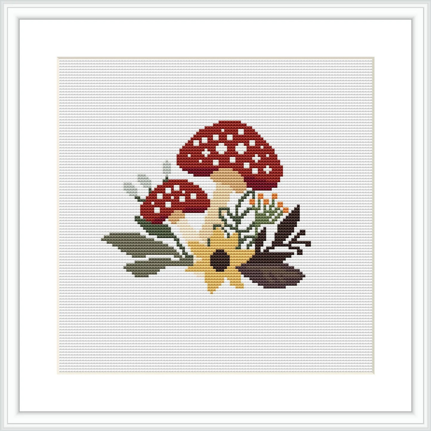 The image depicts a cross stitch pattern of red mushrooms with white spots on their caps, accompanied by autumn leaves predominantly in shades of yellow, green, and brown. The design is showcased against a white fabric background, simulating how it would look when completed.